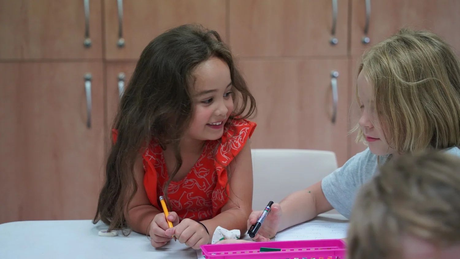 Two girls smiling as they draw together at the Children’s Church craft table at CoastWIDE