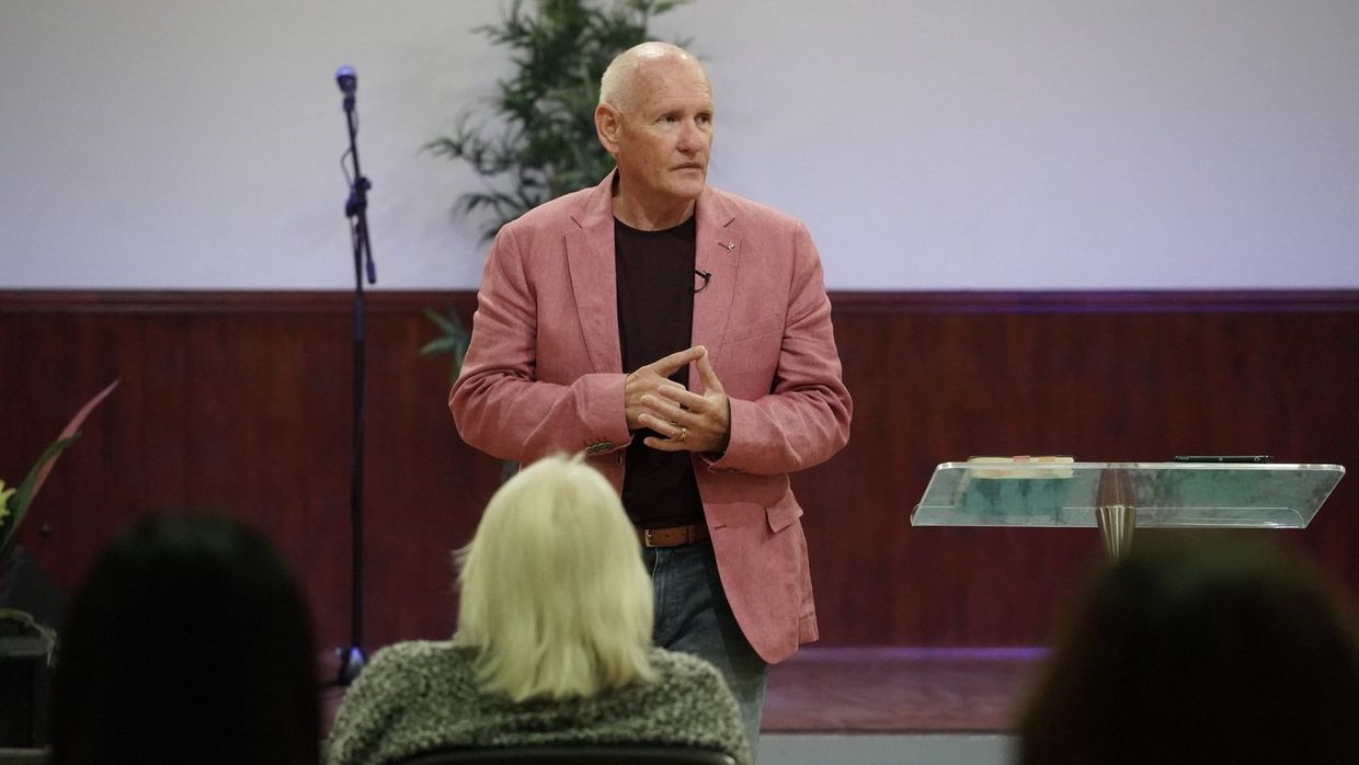 Pastor Shayne preaching in a pink jacket, the congregation in the foreground