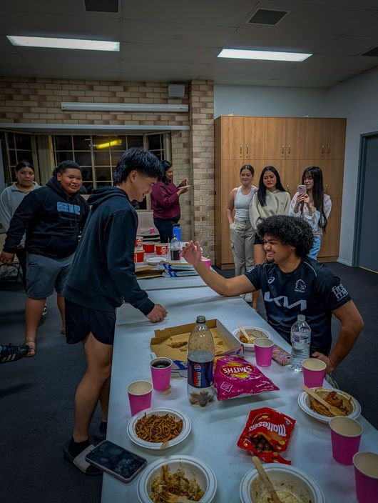 Young adults share pizza and snacks around a long table at CoastWIDE Church