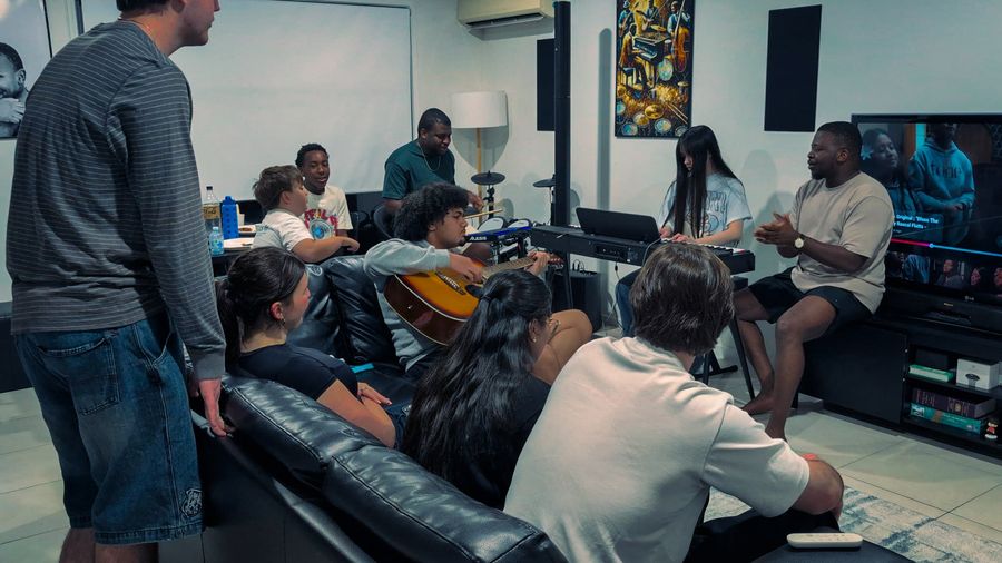 Young adults hang out together on couches, one playing guitar, at a CoastWIDE Young Adults night