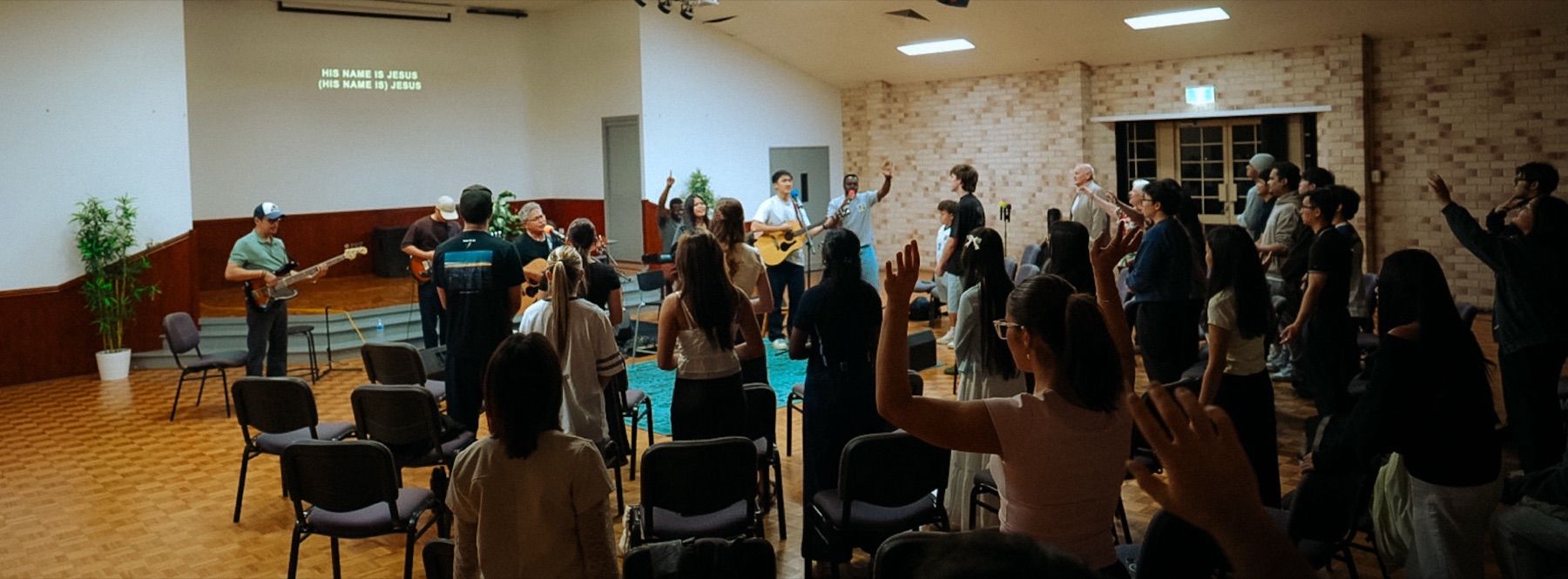 Young people worship with hands raised as the Young Adults band leads at CoastWIDE Church, Arundel